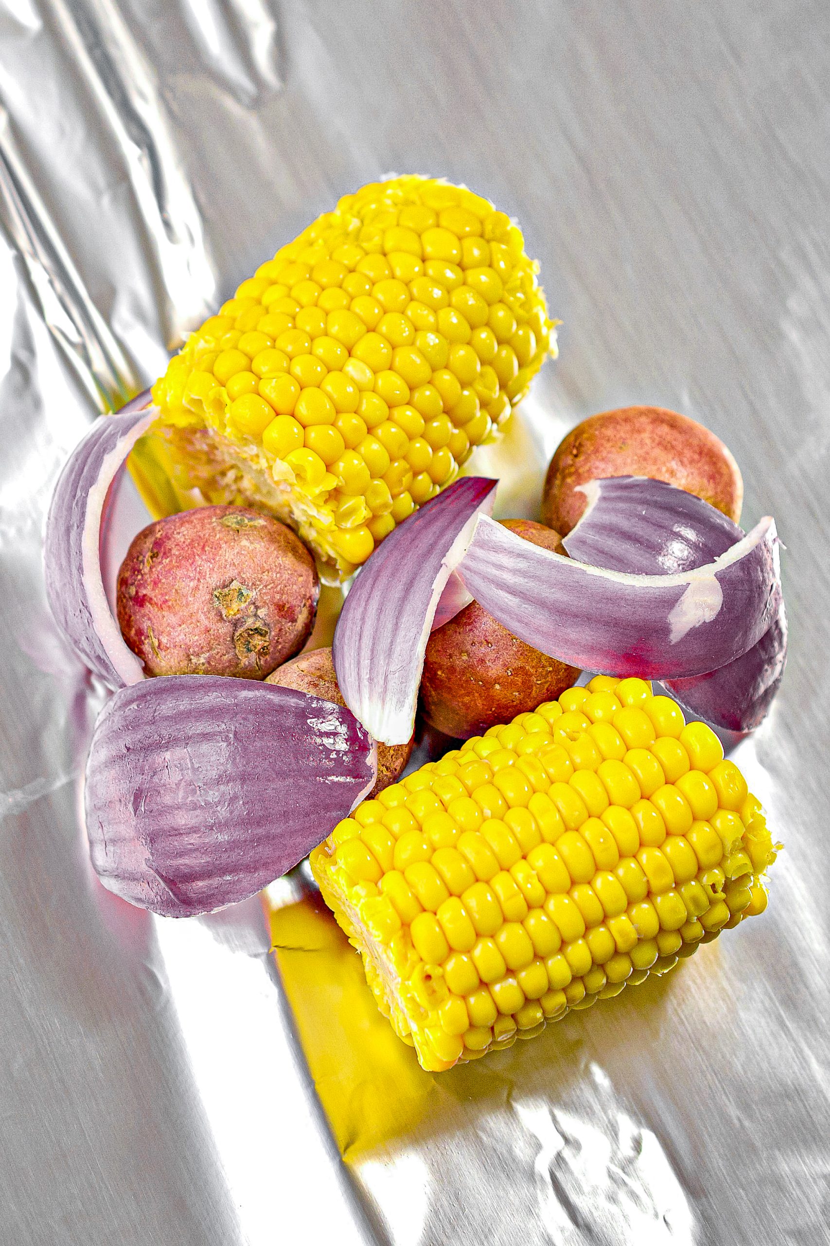 In the center of each sheet of foil, place two pieces of corn on the cob, four baby potatoes, ¼ of the shrimp, ¼ of the sausage, some red onion, red bell pepper, salt, and pepper to taste, and cajun seasoning to taste.