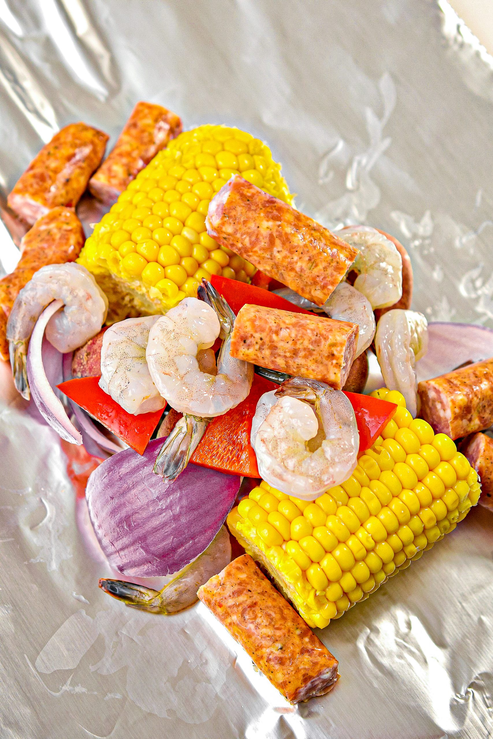 In the center of each sheet of foil, place two pieces of corn on the cob, four baby potatoes, ¼ of the shrimp, ¼ of the sausage, some red onion, red bell pepper, salt, and pepper to taste, and cajun seasoning to taste.