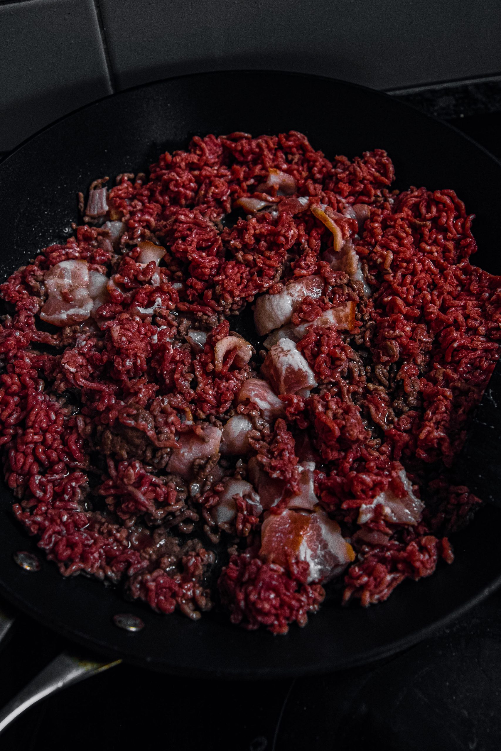 In a large, wide skillet, add the bacon and ground beef. Stir constantly and cook over medium-high heat until golden brown.