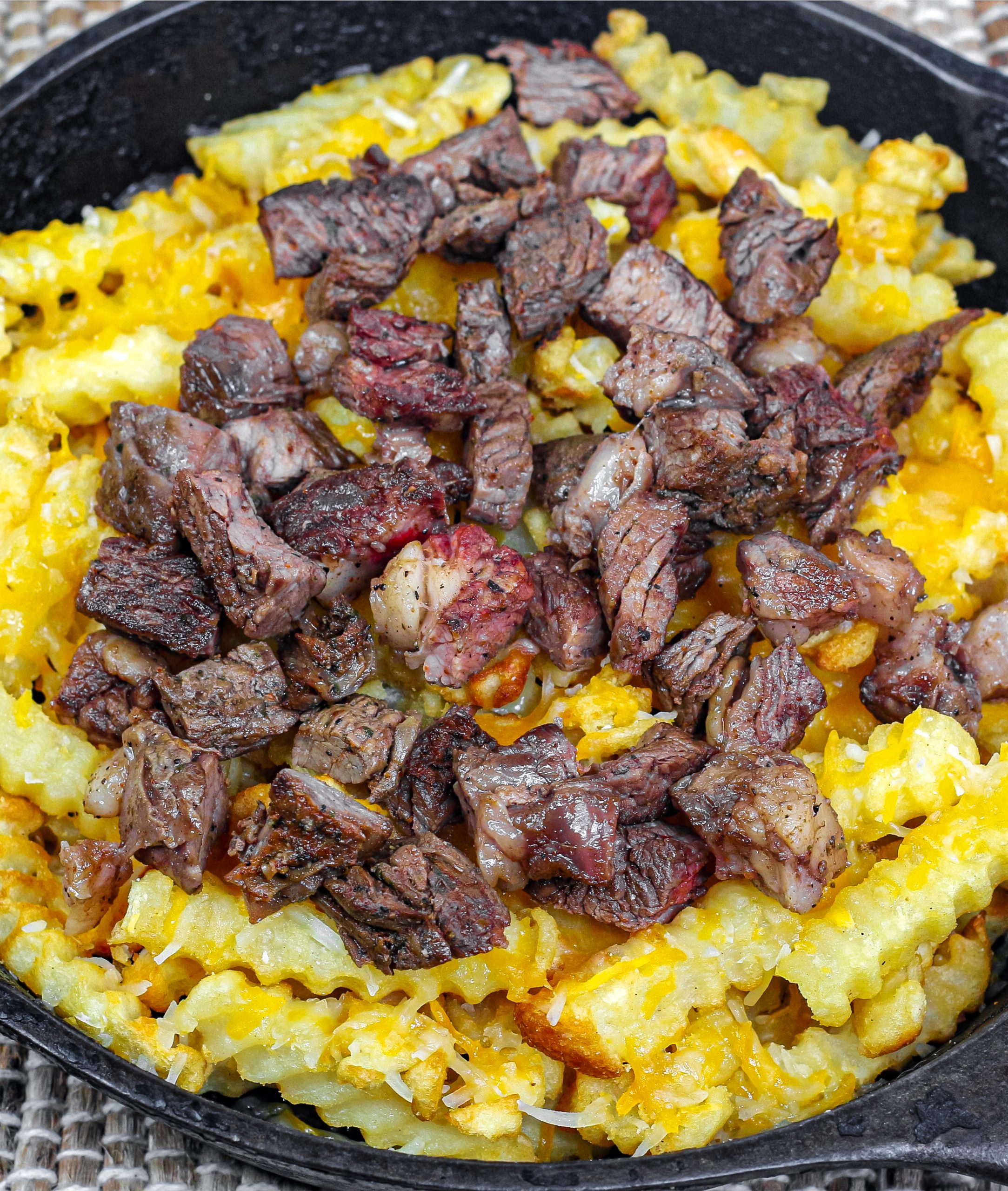 Using a castiron skillet, place the baked french fries, Mexican shredded cheese, and diced carne asada, then broil until the cheese is melted.
