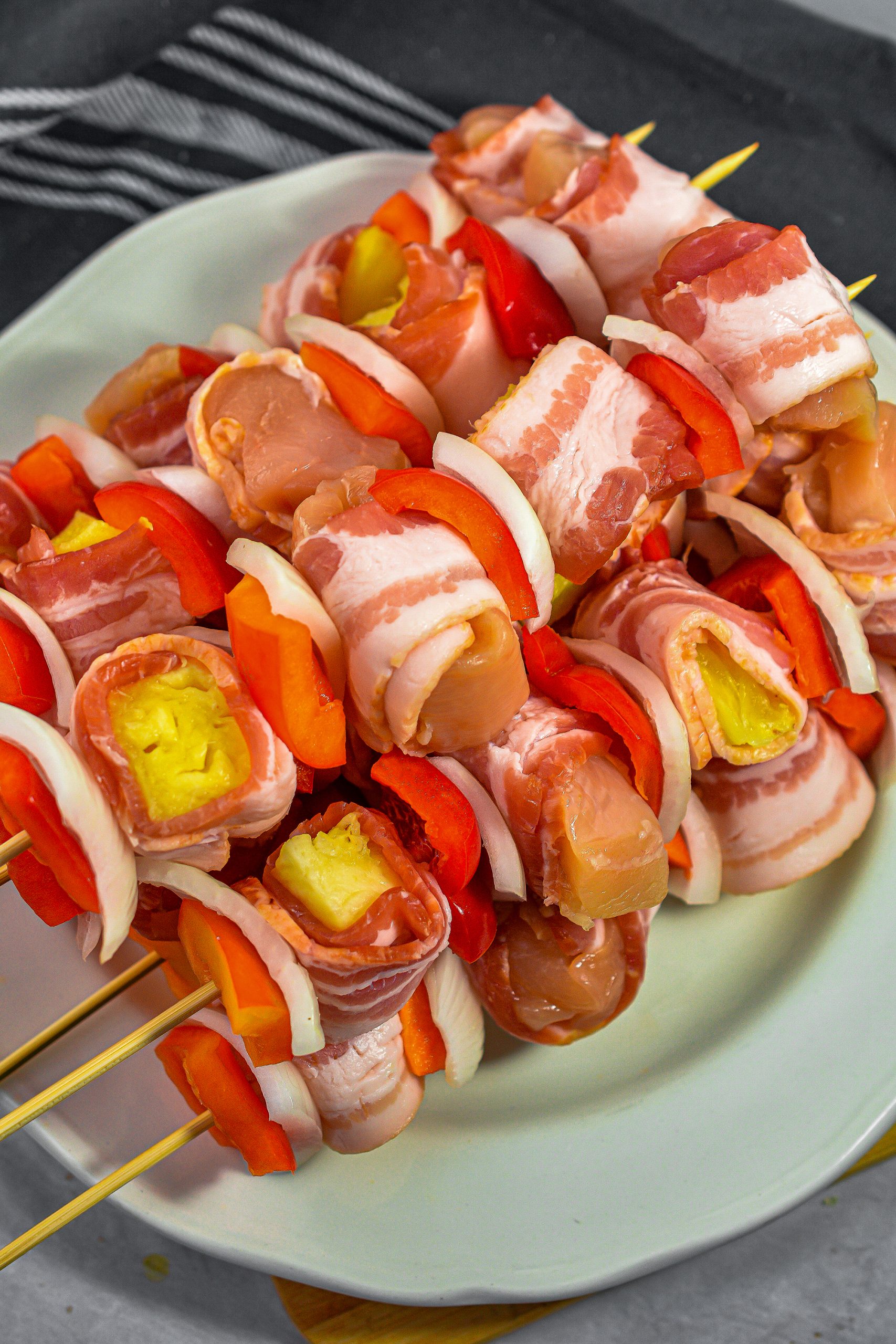 Thread pieces of the red pepper, onion, bacon-wrapped chicken, and pineapple on the skewers.