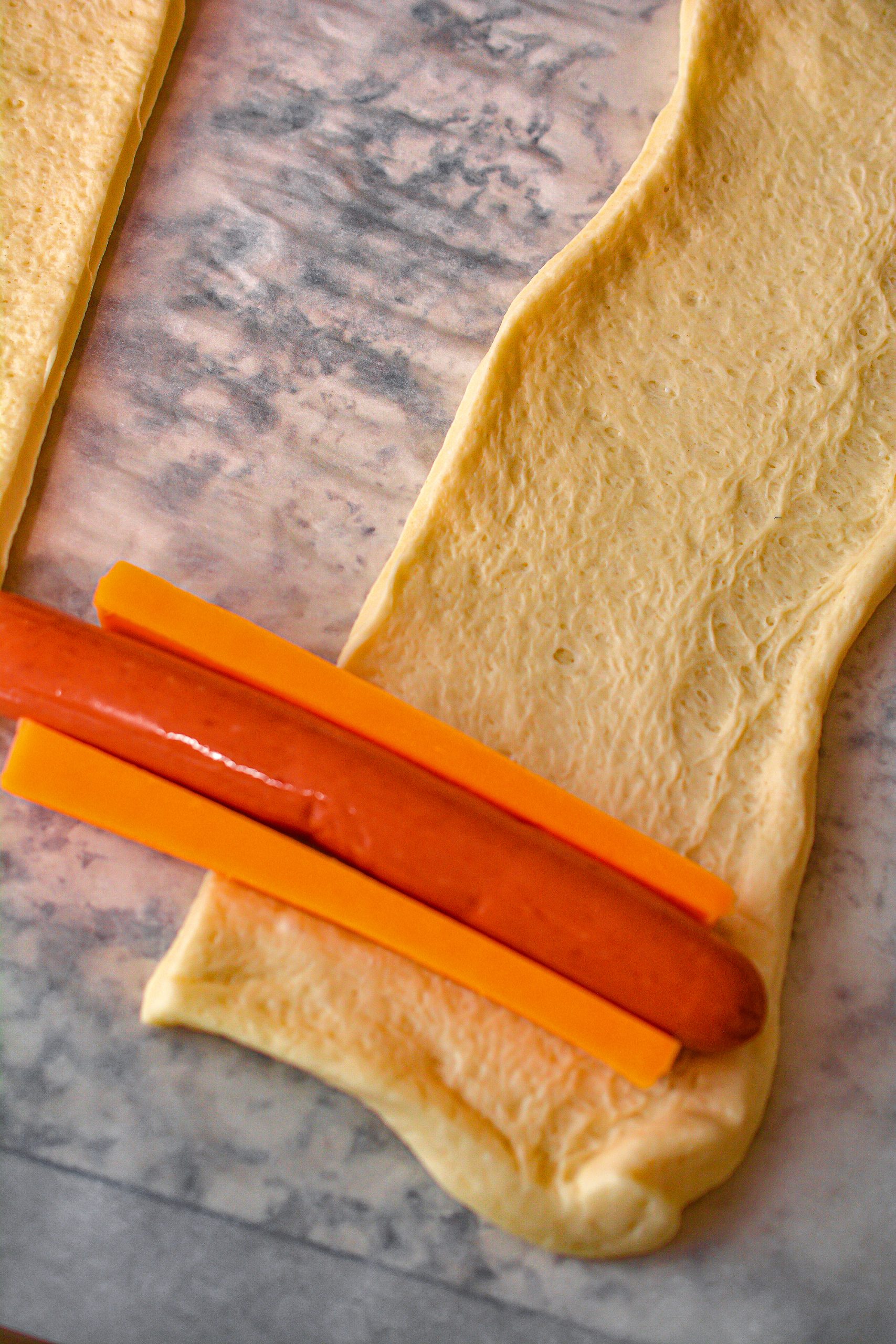 Add a hot dog with one piece of cheese stick on each side to one end of a piece of dough, and roll the dough around the hot dog and cheese sticks, overlapping the layers as you go.