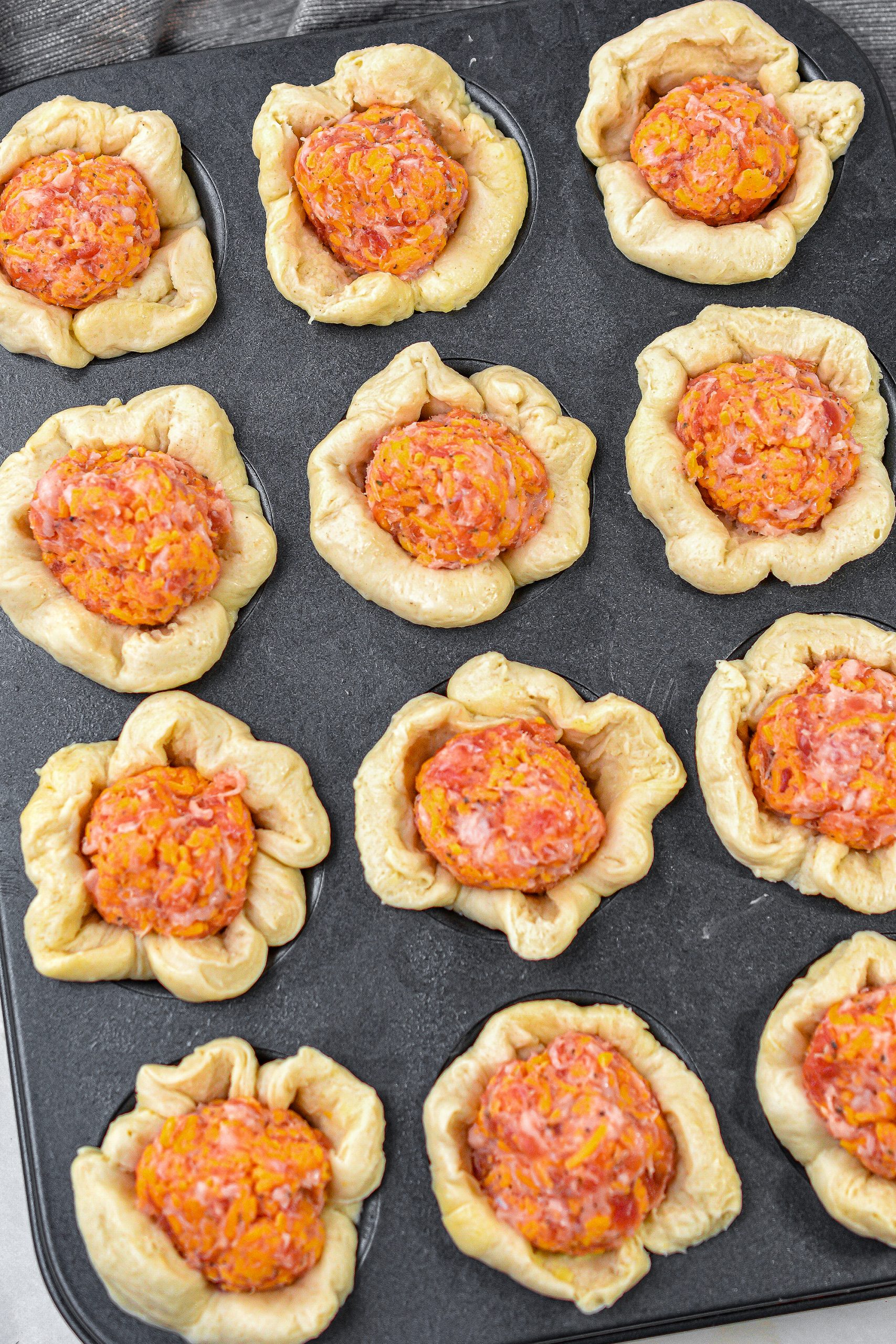 Press a ball of sausage into the center of each dough cup in the mini muffin tins.