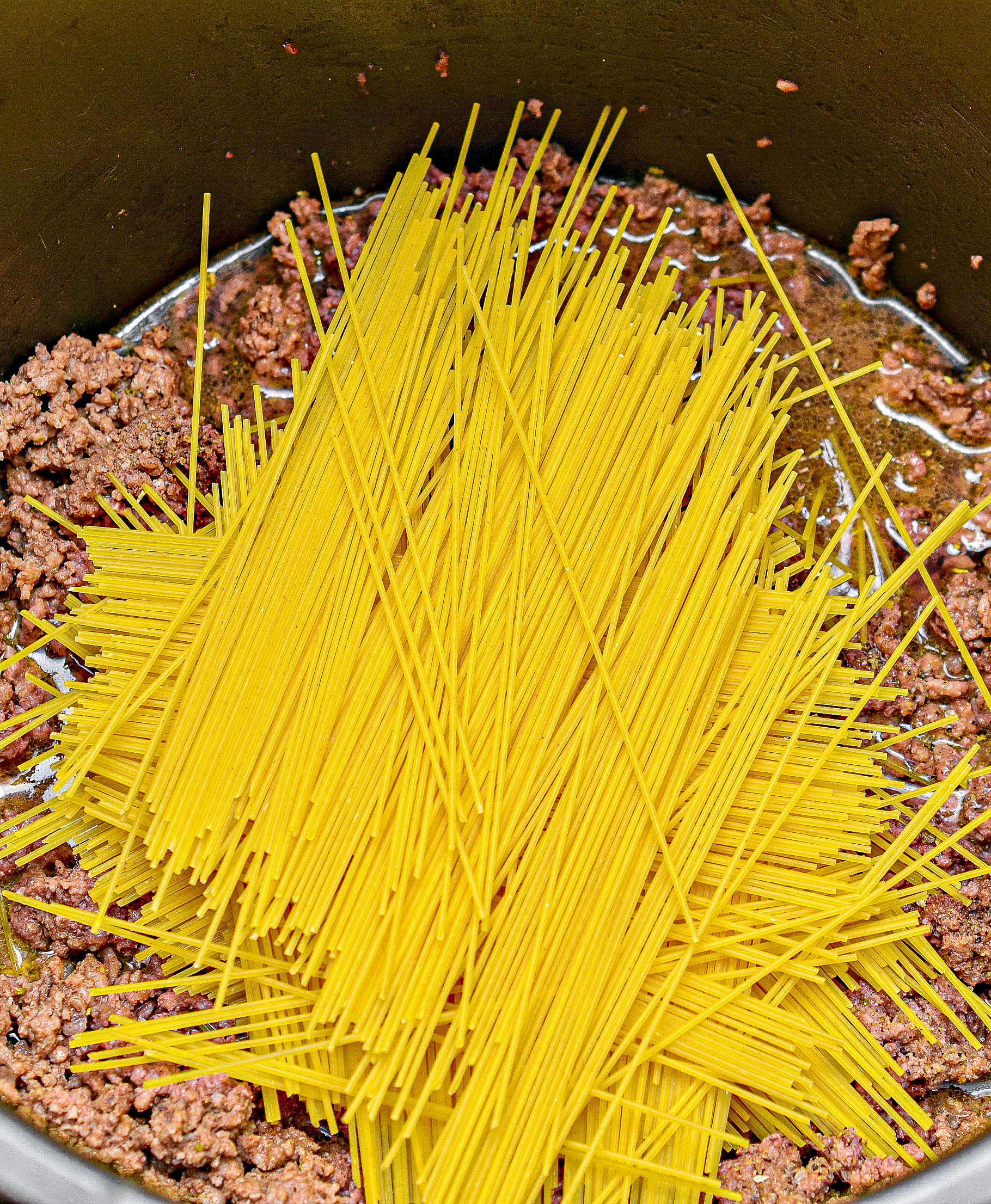 Break the spaghetti noodles in half, and layer them a little at a time on top of the meat mixture in the Instant Pot, layering the noodles in slightly different directions each time.
