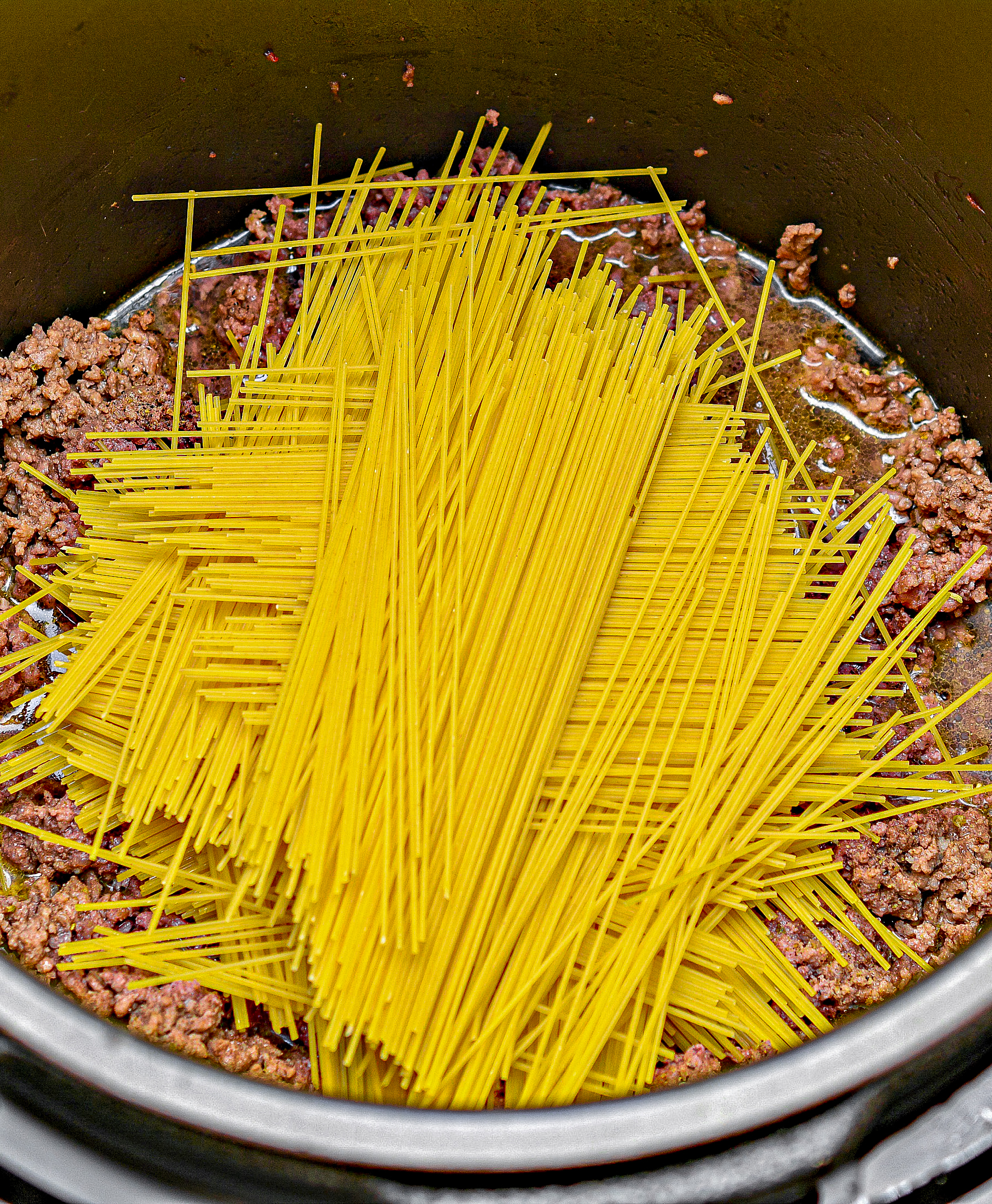 Break the spaghetti noodles in half, and layer them a little at a time on top of the meat mixture in the Instant Pot, layering the noodles in slightly different directions each time.