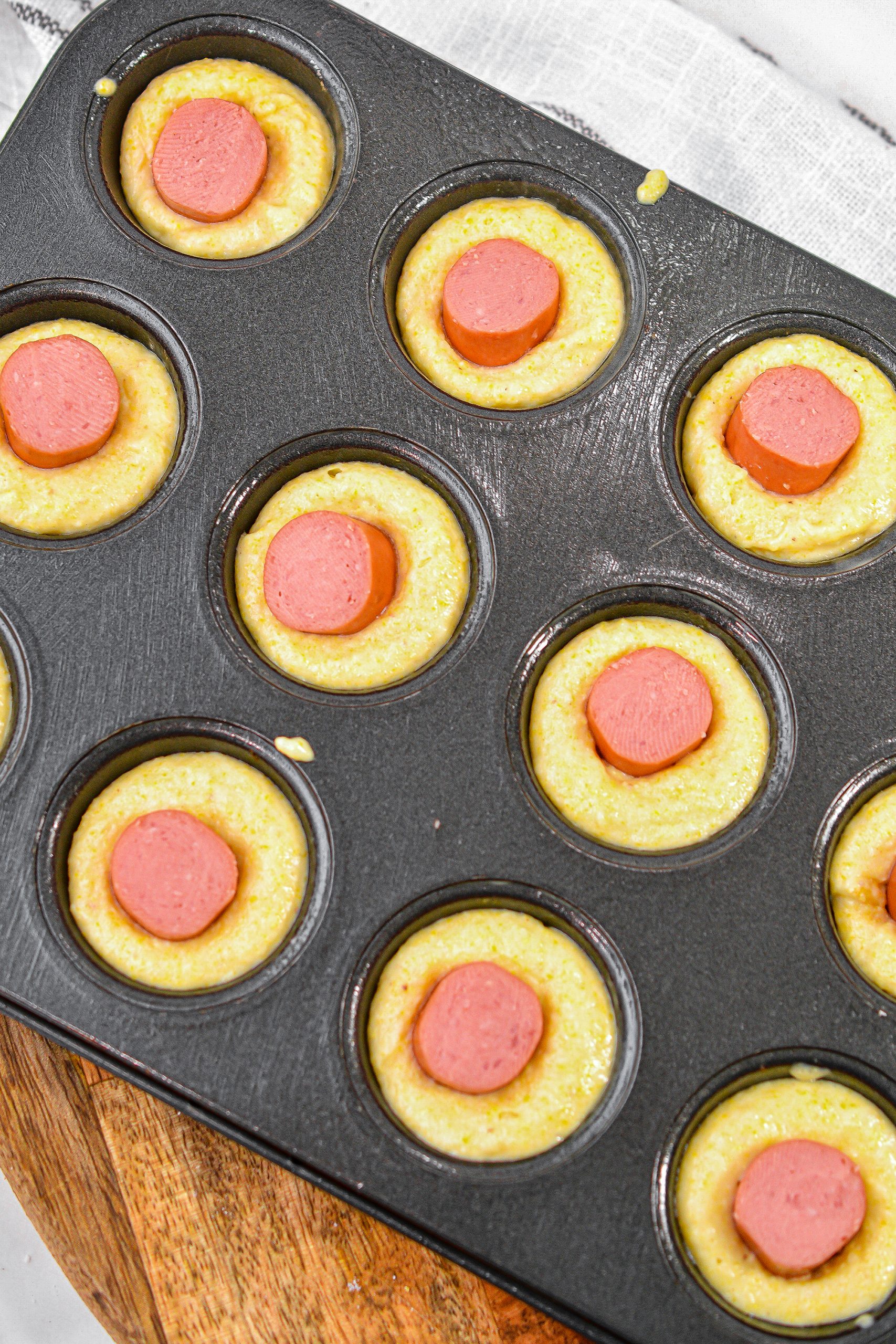 Place a piece of hot dog into the center of each filled section of the mini muffin tin.