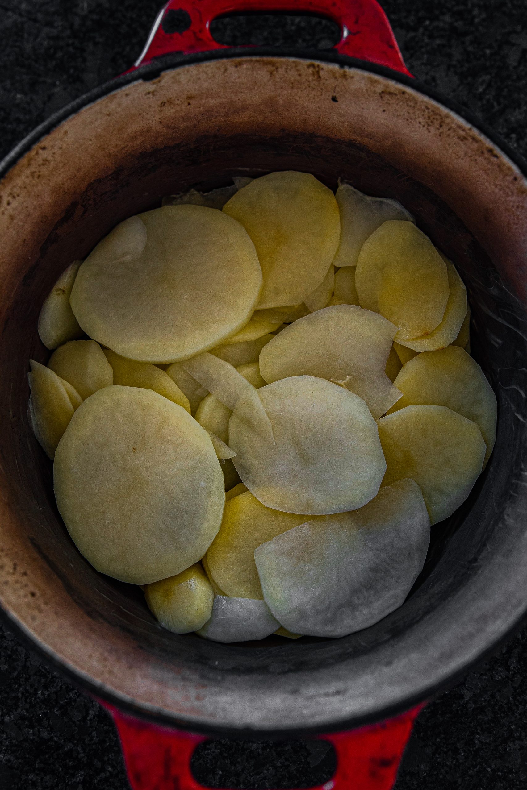 Butter a separate saucepan, and place the potatoes stacked on top of each other. 