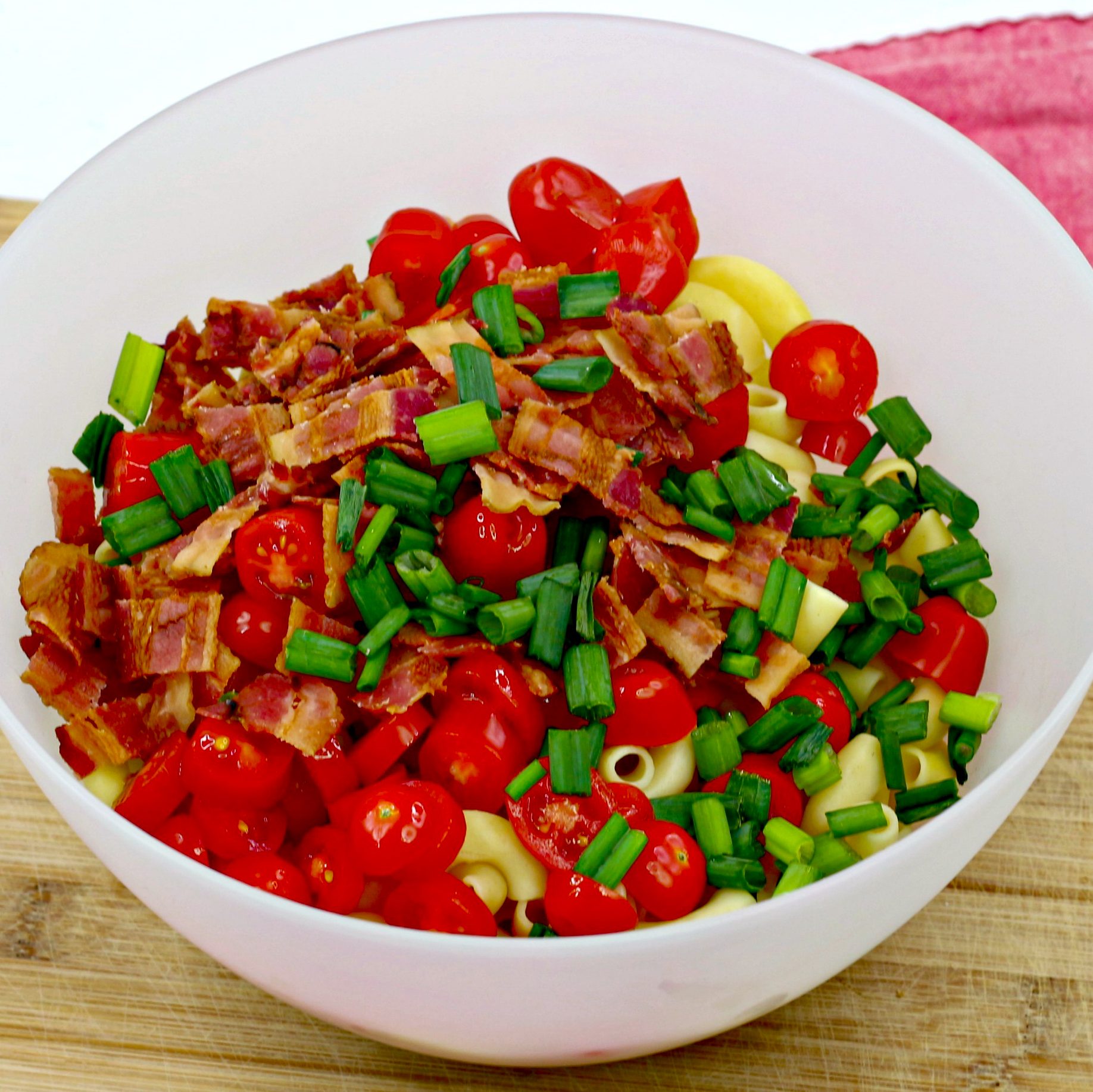 In a large bowl, add the cooked pasta, crumbled bacon, sliced tomatoes, and green onions.